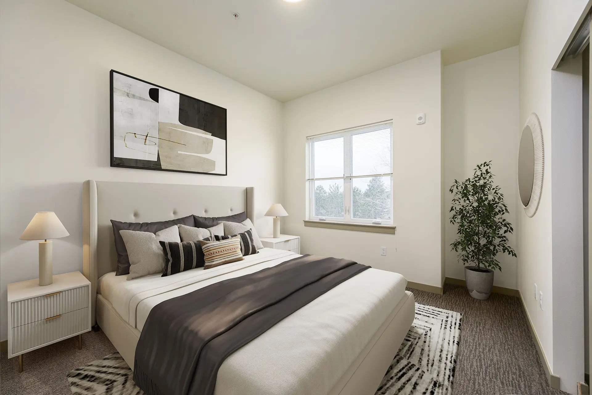 Bedroom with a large bed decorated with several pillows and abstract art hanging above it. To the left of the bed there is a large window and a bump out with a potted plant on the floor