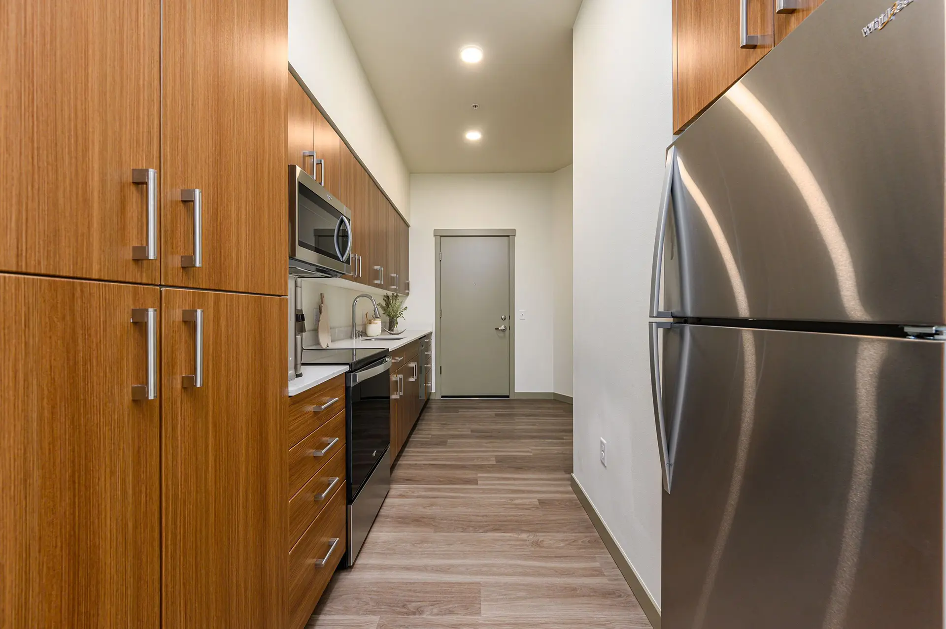 Galley kitchen with custom cabinets, built-in pantry, wood style flooring and stainless appliances