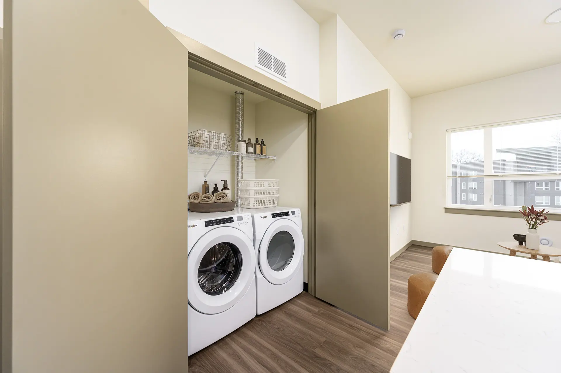 double door utility closet beside the kitchen. The closet has a wire shelf with full sized front loading washer and dryer inside.