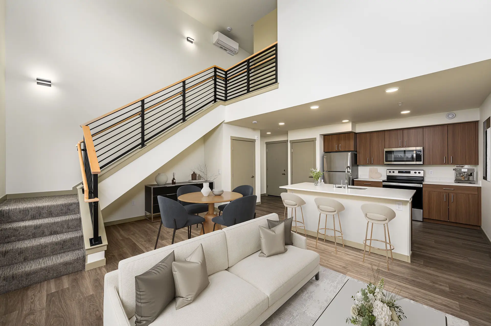 living room with couch, small dining table, three bar stools at the kitchen island, and open carpeted stairwell leading to the loft bedroom