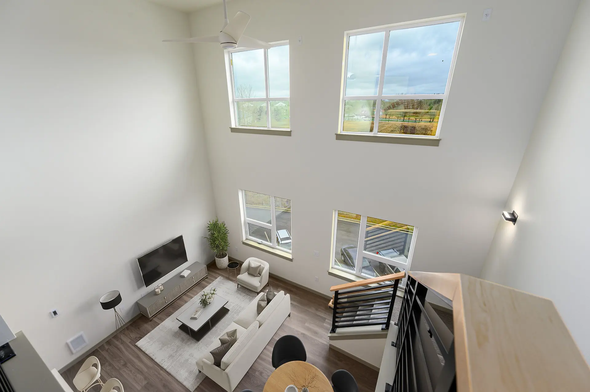 birds eye view of living room from a loft stairwell landing. The far wall has four large windows stacked in rows of two.