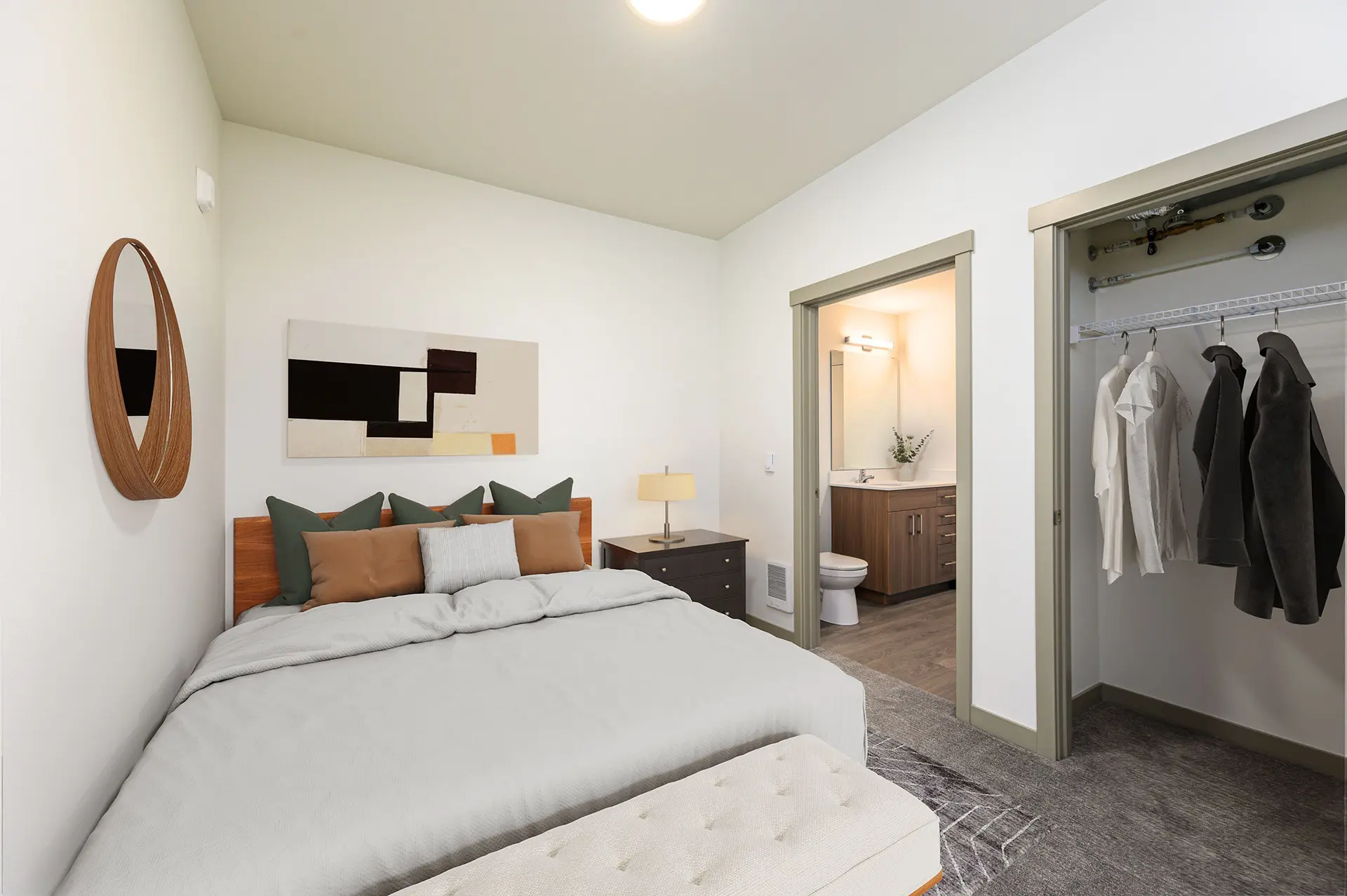 carpeted bedroom with large bed against the wall, closet on the right with the door open, and door leading to bathroom en suite.