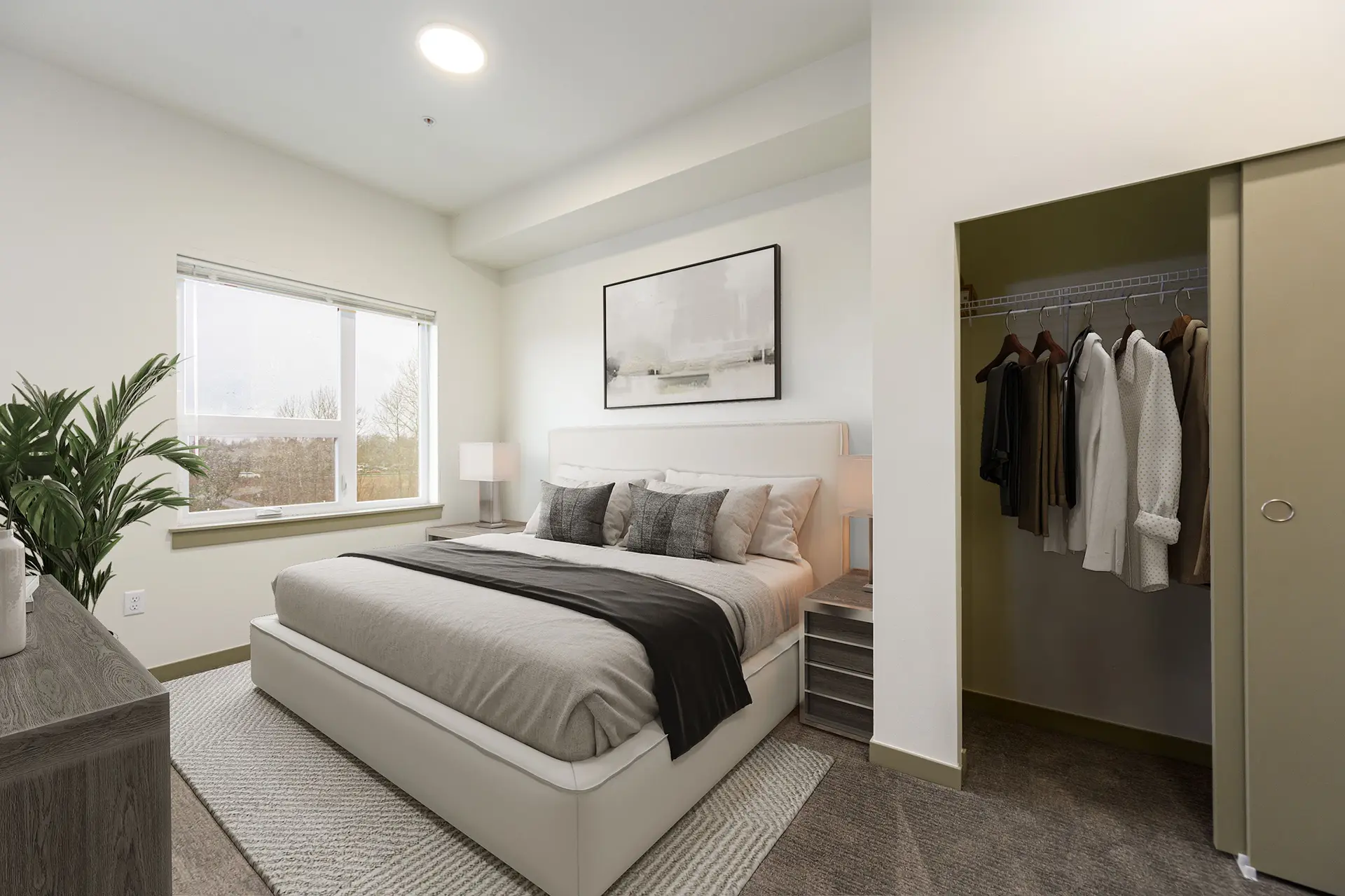 carpeted bedroom with large bed next to a wide window on the left, and closet with sliding door on the right. The walls are white and the doors are tent green.