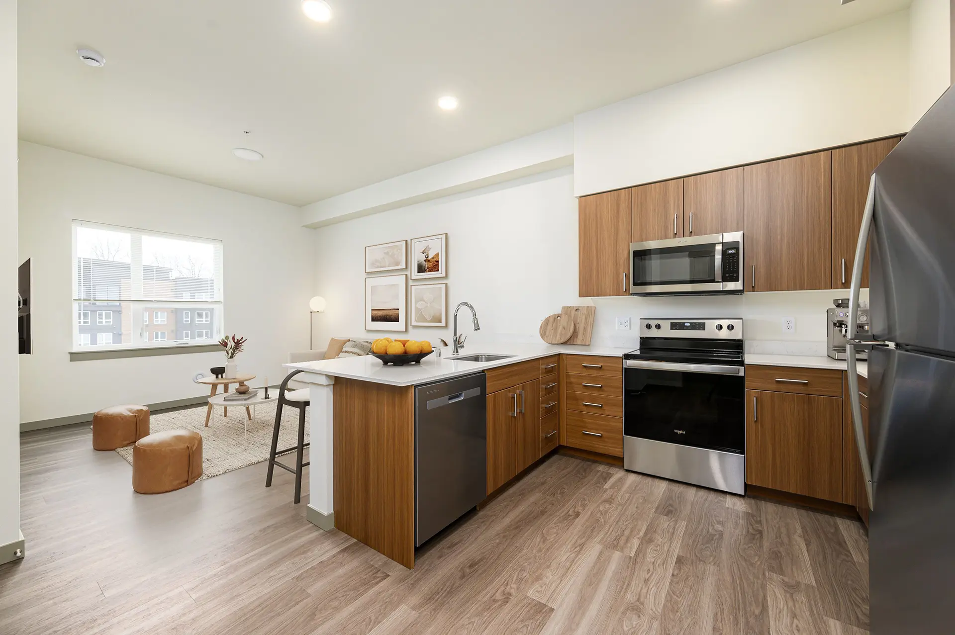 kitchen with large countertop open to the living room which has a wide window, couch, two round cushion seats, and a wall mounted TV