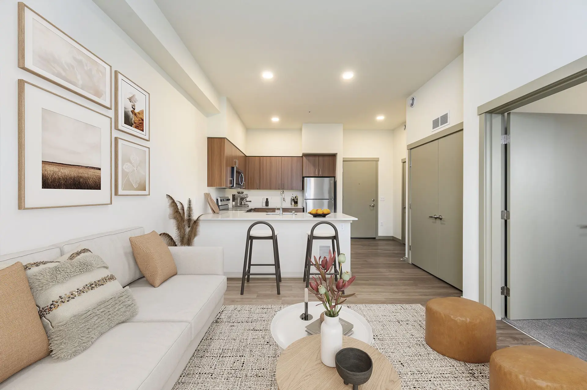 view of kitchen from living room with a large off-white couch and round cushion seats on a rug, open door to a carpeted bedroom to the right, and closed utility room double-door closet next to the kitchen.