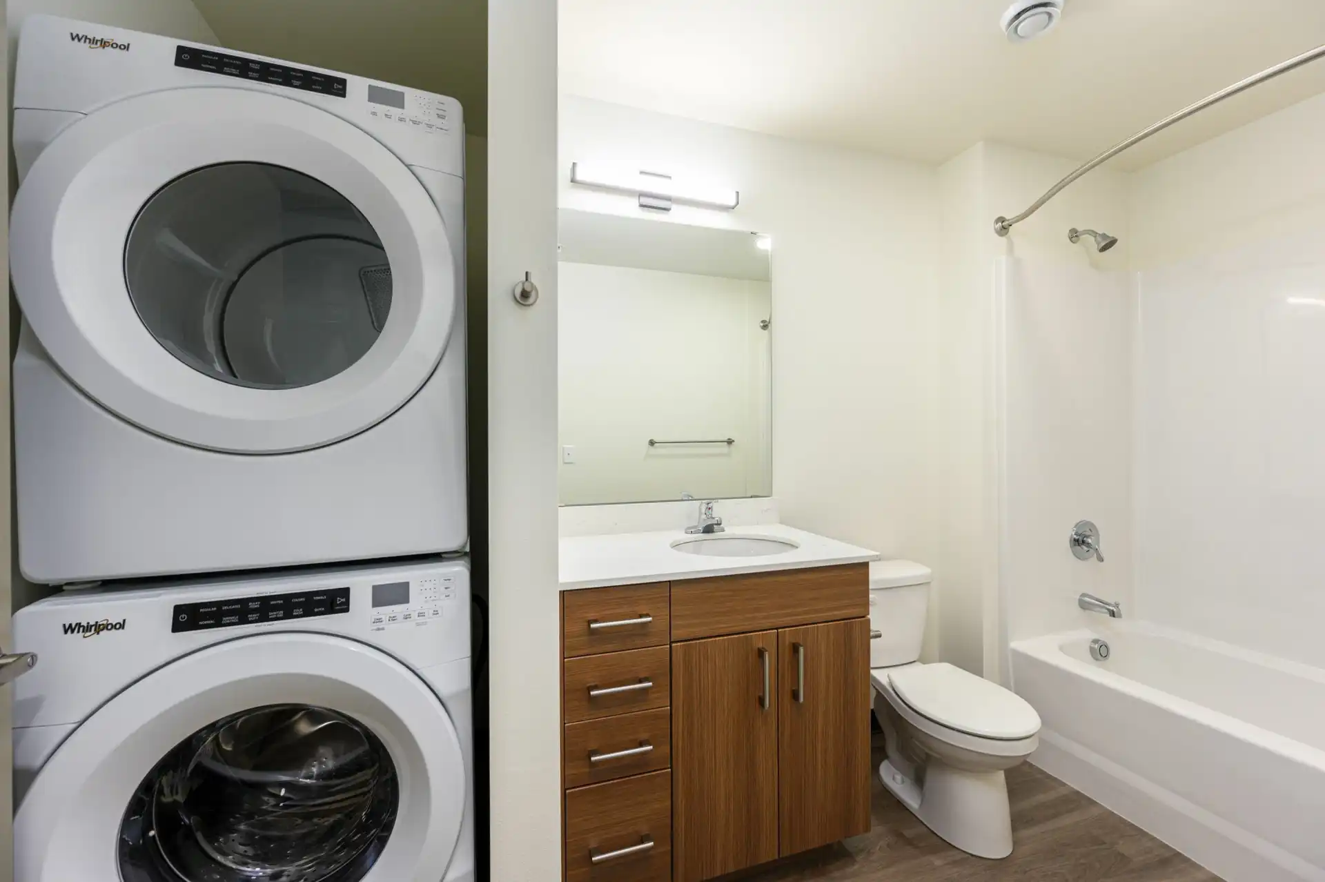 bathroom with single vanity, toilet, tub with curve shower rod, and closet with stacked front loading washer and dryer.