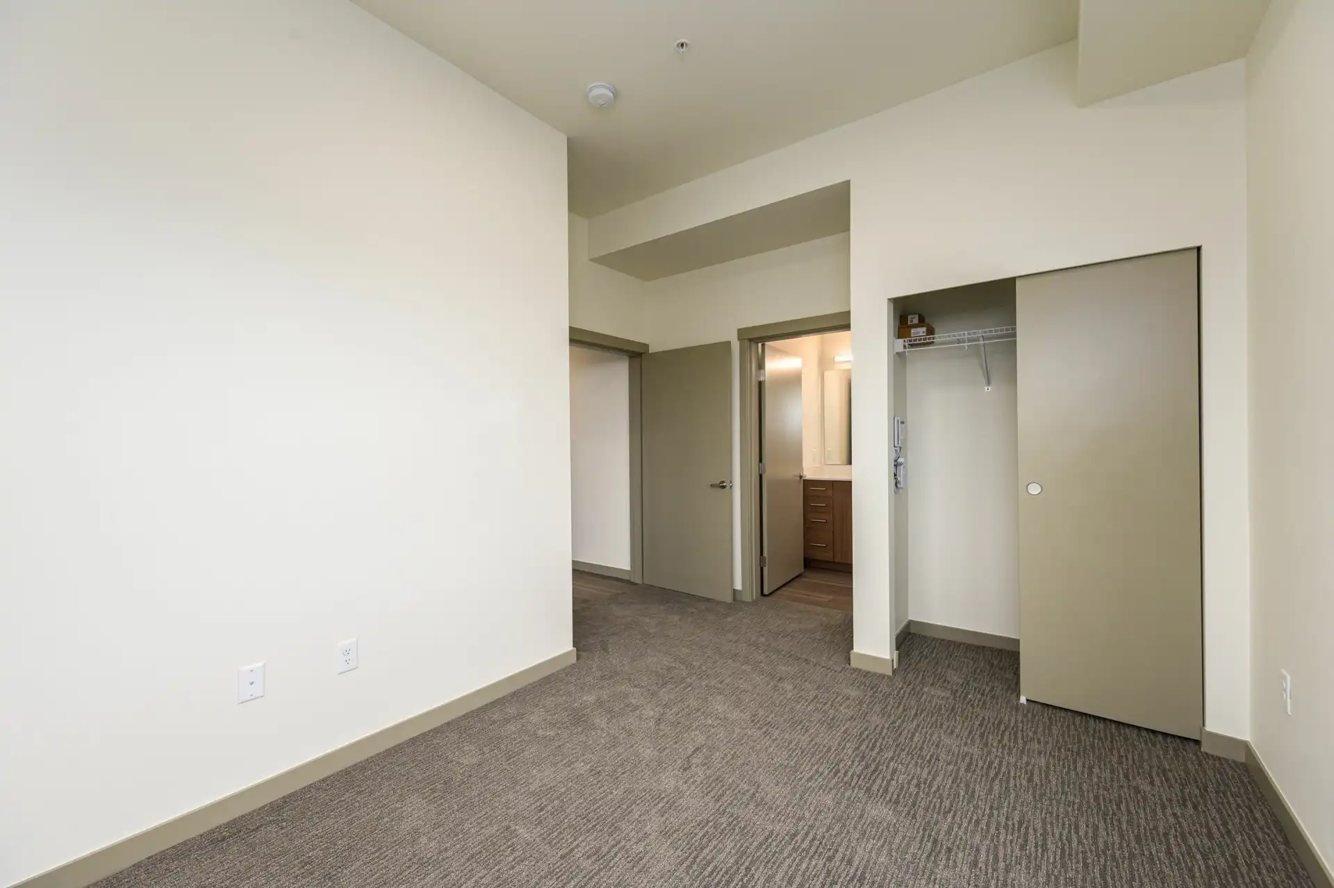 carpeted bedroom with white walls, tent green trim, a door open to the en suite bathroom, and closet with sliding door.