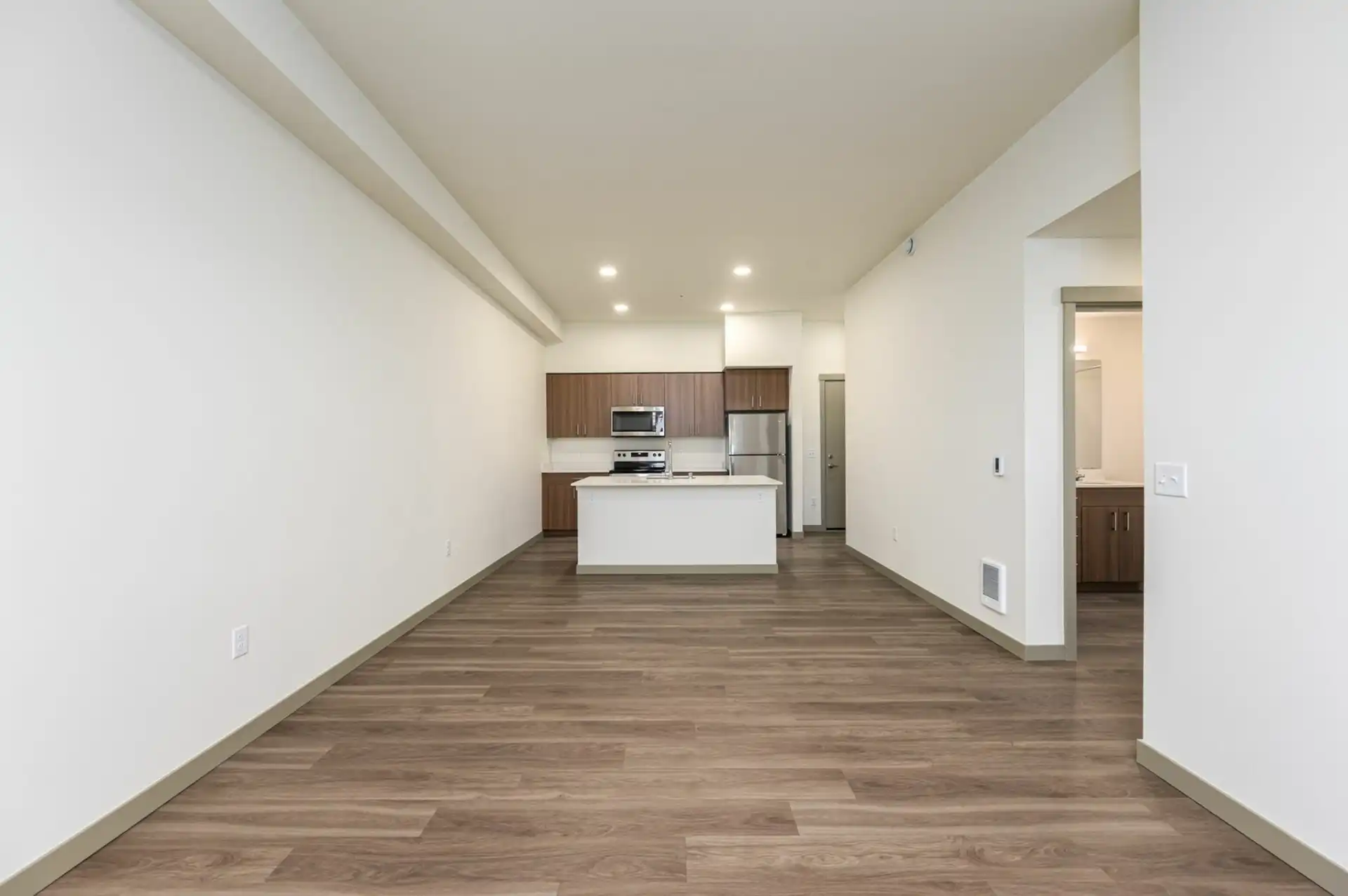 view of open kitchen from the living room with wood style flooring throughout, stainless appliances, large island, and custom cabinets.