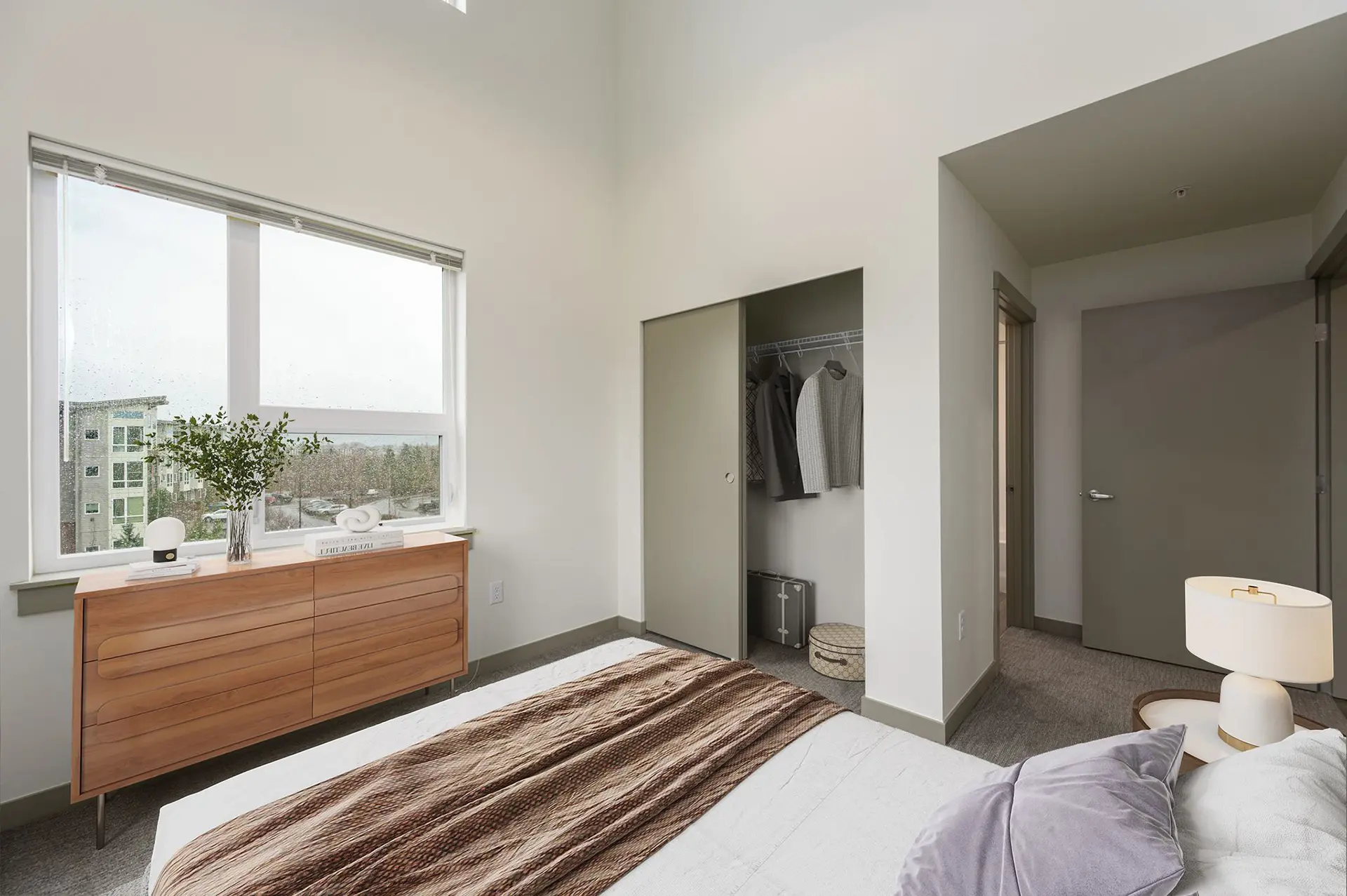 carpeted bedroom with large bed facing a window, high ceilings, and a closet with sliding door.