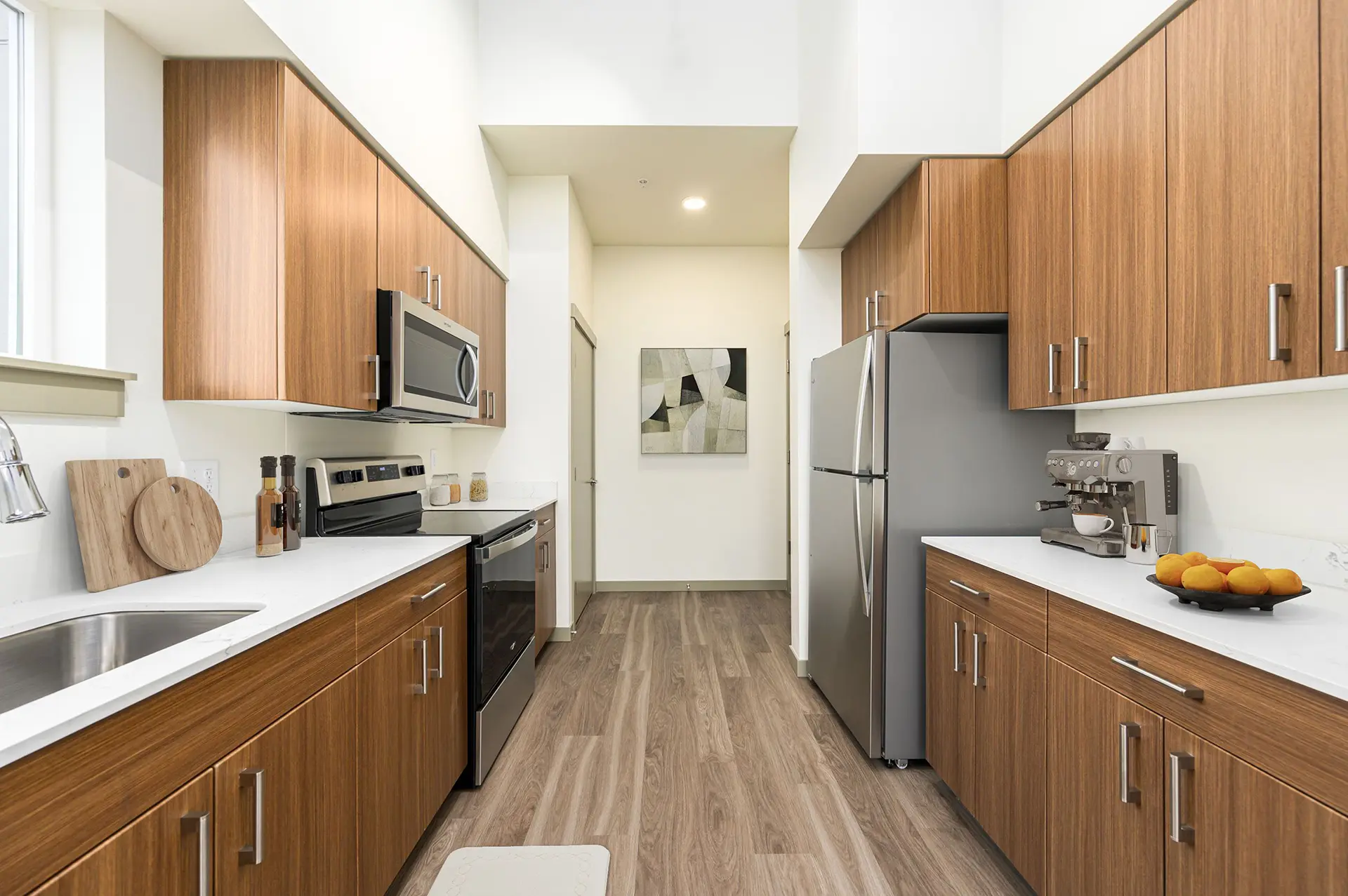 large galley kitchen with luxury cabinets, brushed nickel hardware, white countertops, stainless appliances, and a glasstop stove. A large espresso machine sits on the counter next to the refrigerator leaving plenty of room around it for workspace.