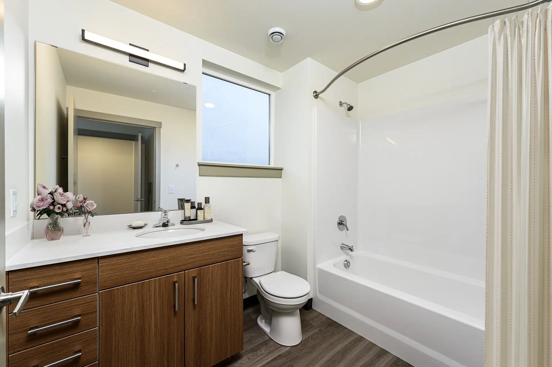 bathroom with single vanity with large white countertop, luxury cabinets, square window above the toilet, and shower/tub combo with curved shower rod.