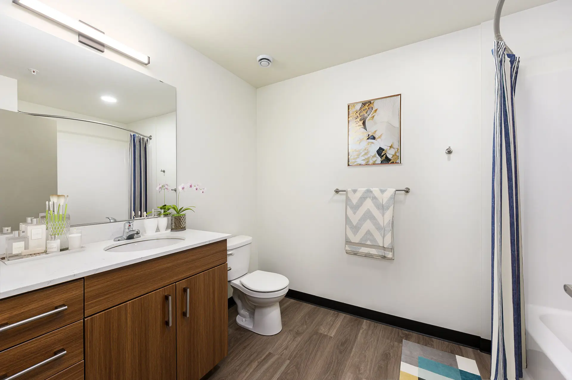 bathroom with wood flooring, black baseboard, single vanity with long white countertop, luxury cabinets with brushed nickel hardware, and tub with curved shower rod.