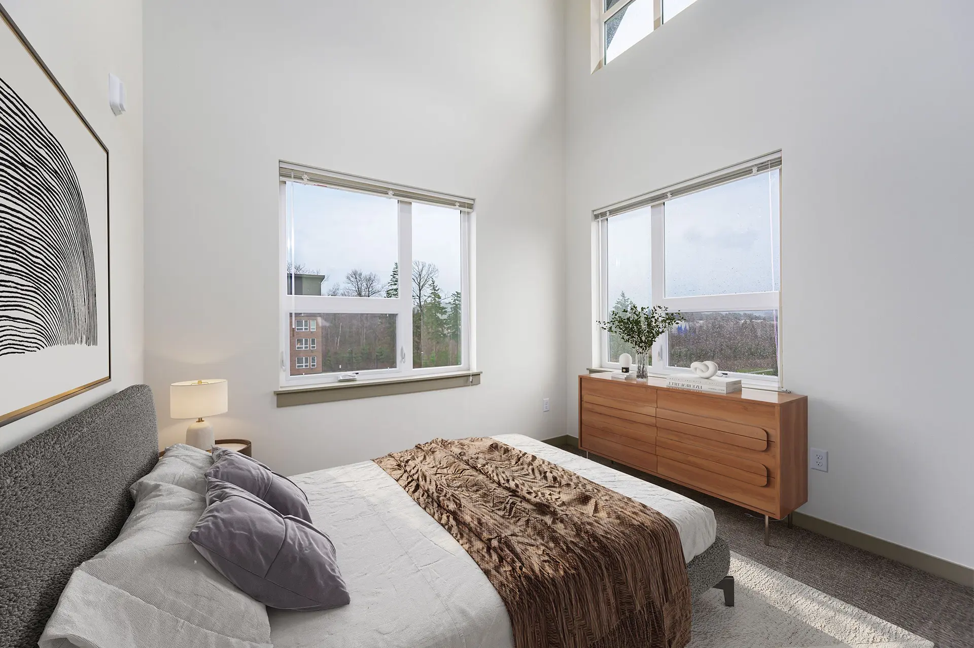 gray carpeted bedroom with high ceiling, white walls, a king sized bed looks out to three large windows, one near the top of the ceiling.