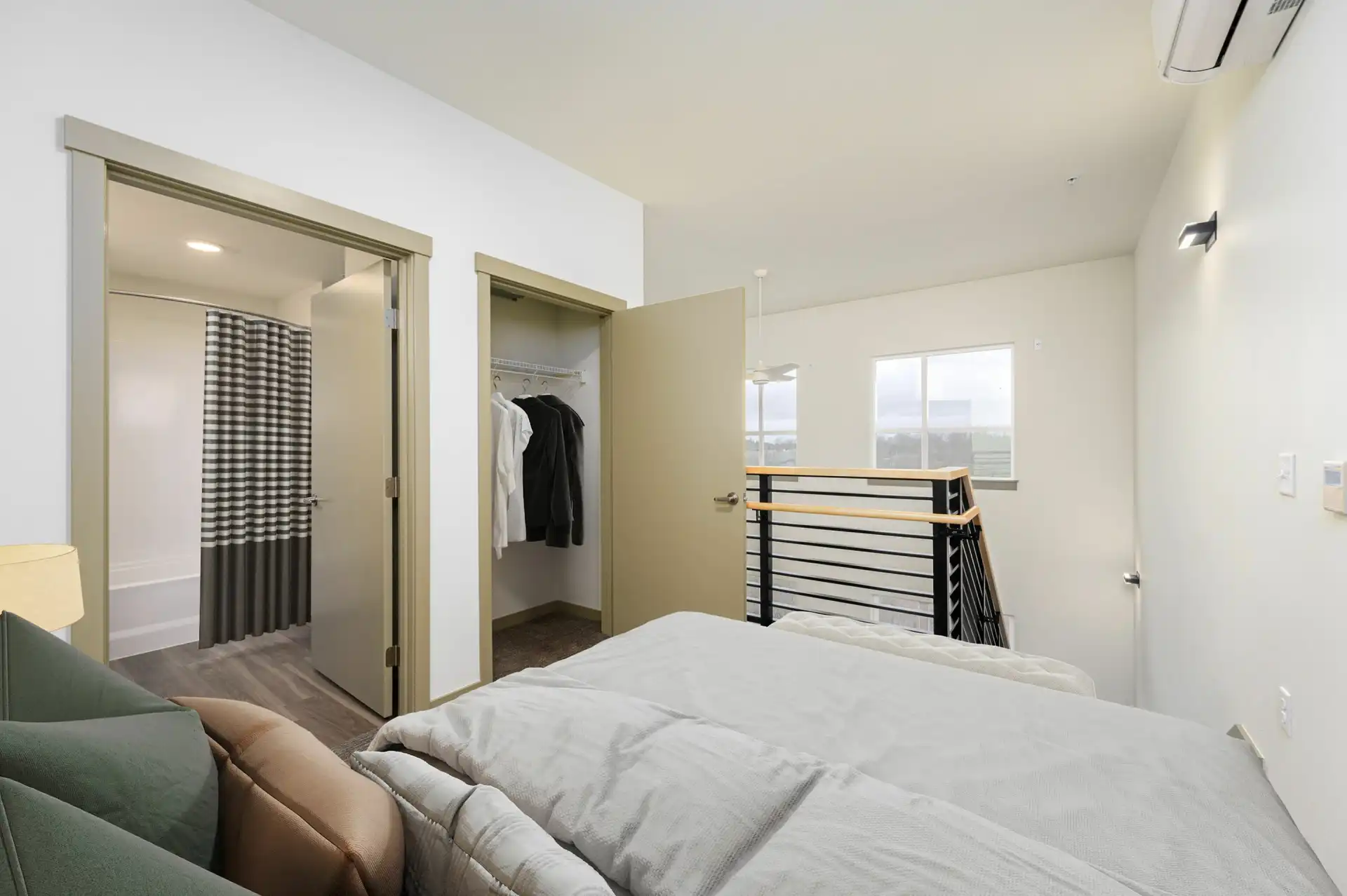 bedroom in a loft with view of two large windows in the stairwell, en suite bathroom on the left next to a closet with an open door.