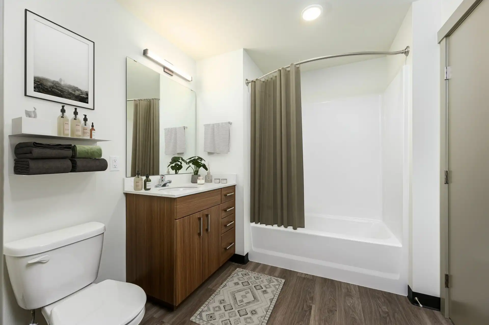 bathroom with toilet next to single vanity, thin white minimalist shelves above the toilet, and tub with curved curtain rod.