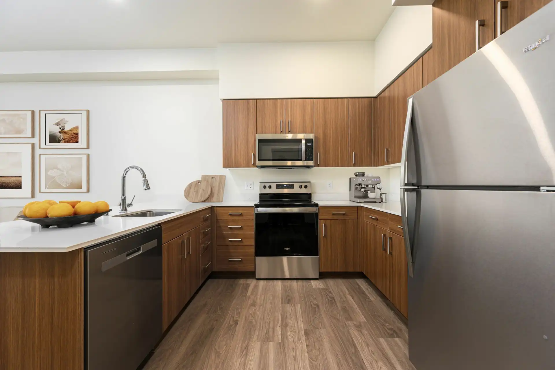 U-shaped kitchen with wood style flooring, custom brown cabinets with brushed nickel hardware, stainless appliances, sink in the bar counter to the left and glass top stove with microwave hood in the middle