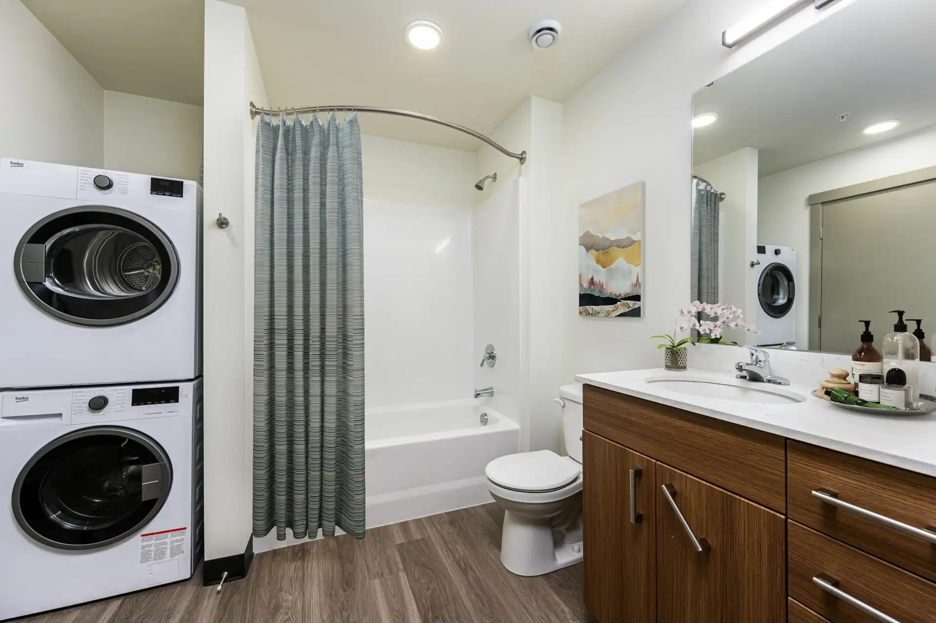 bathroom with single vanity with white countertop and brown cabinets, tub with curved shower rod, stacked front loading washer and dryer.