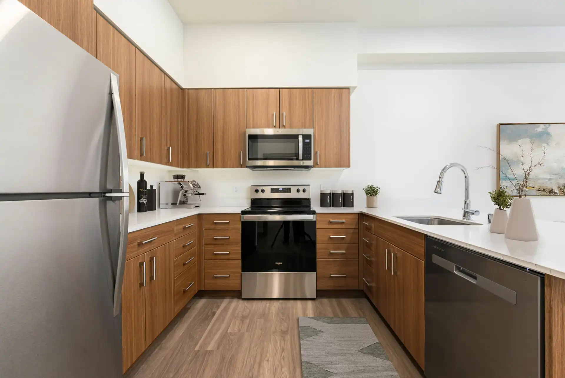 U-shaped kitchen with custom cabinets, white countertops, wood style flooring, refrigerator on the left, stove and microwave hood in the middle, and sink and dishwasher on the right.