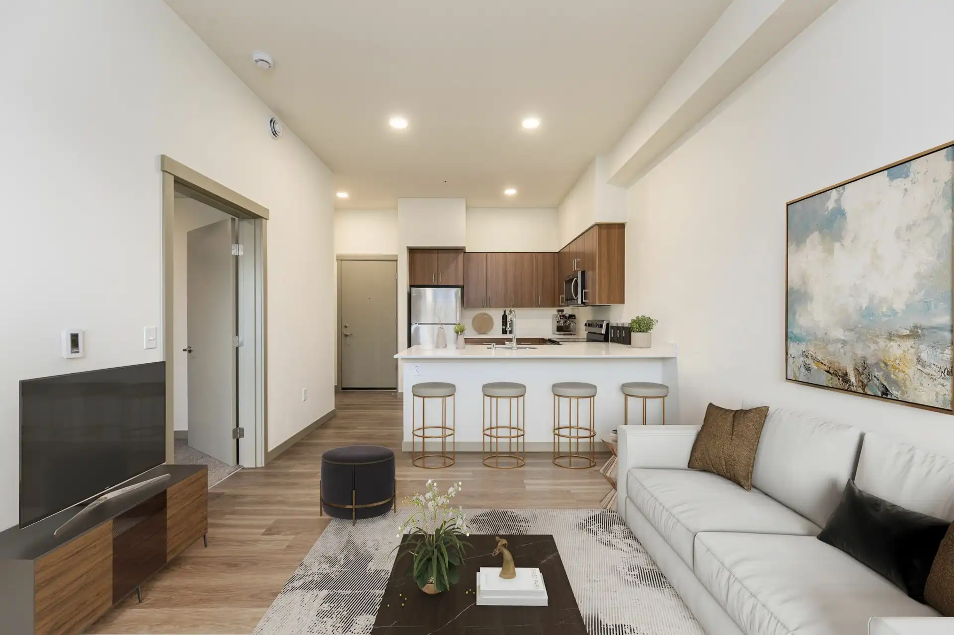 living room with a double couch, TV on a low stand, and open to the kitchen with bar seating for four in the background.